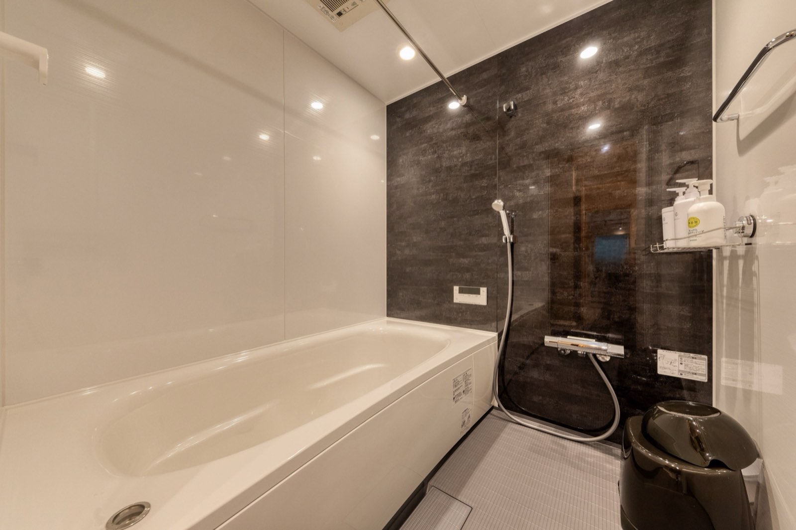 古民家の浴室。白い浴槽と濃色のタイル壁、シャワー