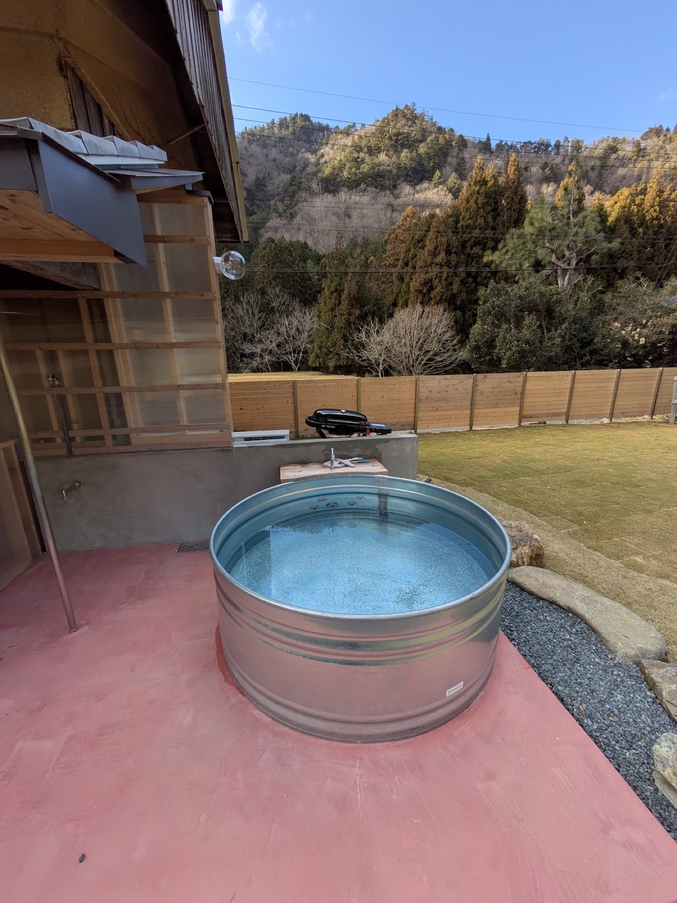 土間に据えられた金属製の水風呂。奥は柵と、色づきはじめた山