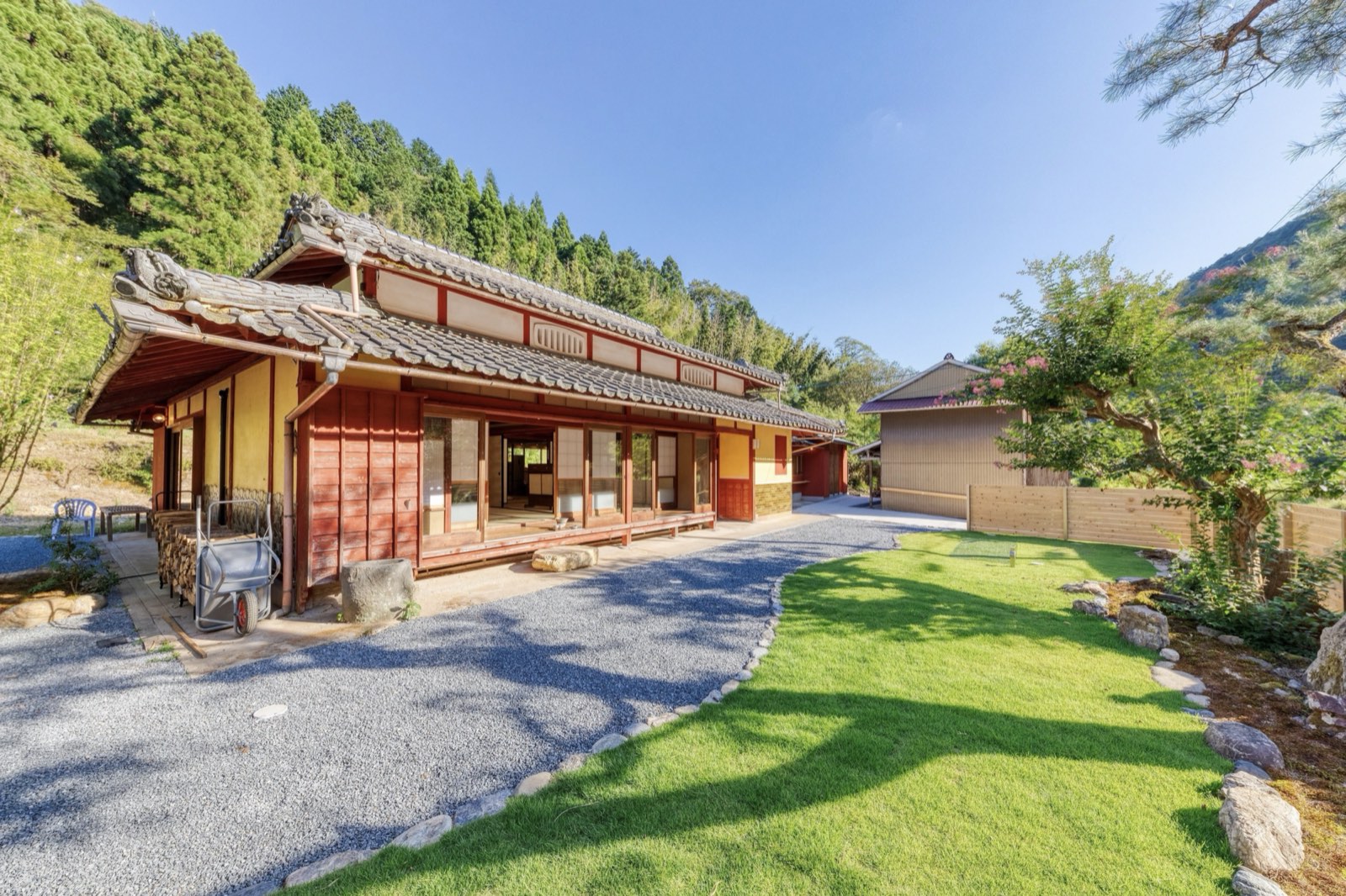 弁柄色の板壁の母屋と、手入れされた芝生の庭。奥に受付棟と山